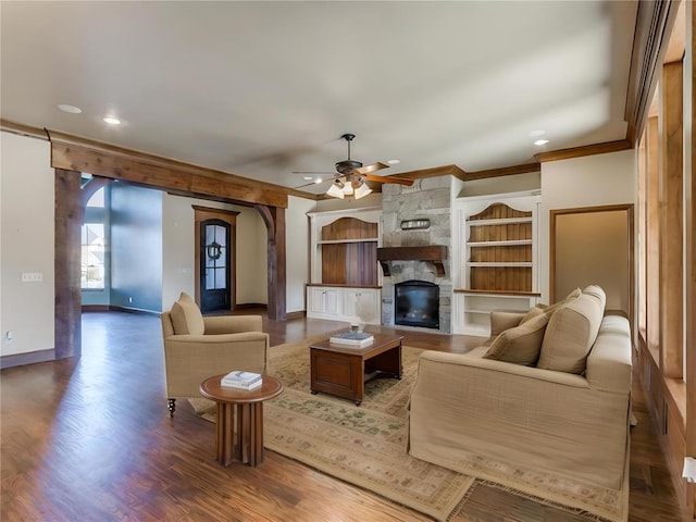 living room featuring crown molding, ceiling fan, wood-type flooring, and a stone fireplace