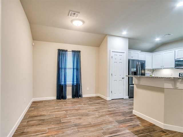 kitchen with vaulted ceiling, white cabinetry, black fridge, and light stone counters