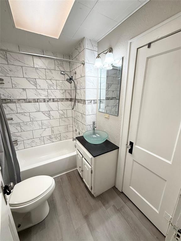 full bathroom with hardwood / wood-style flooring, vanity, shower / bath combination with curtain, and toilet