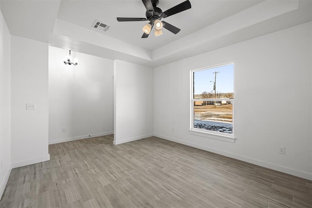 unfurnished room with ceiling fan with notable chandelier, a tray ceiling, and light hardwood / wood-style floors