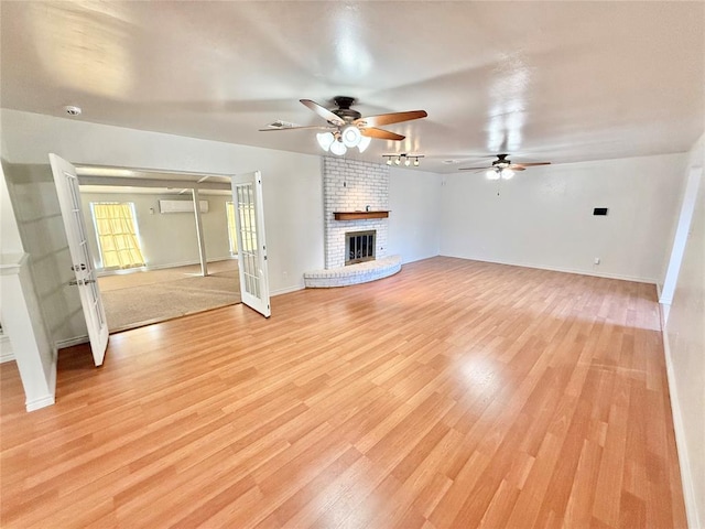 unfurnished living room with ceiling fan, a wall mounted AC, a fireplace, and light hardwood / wood-style flooring