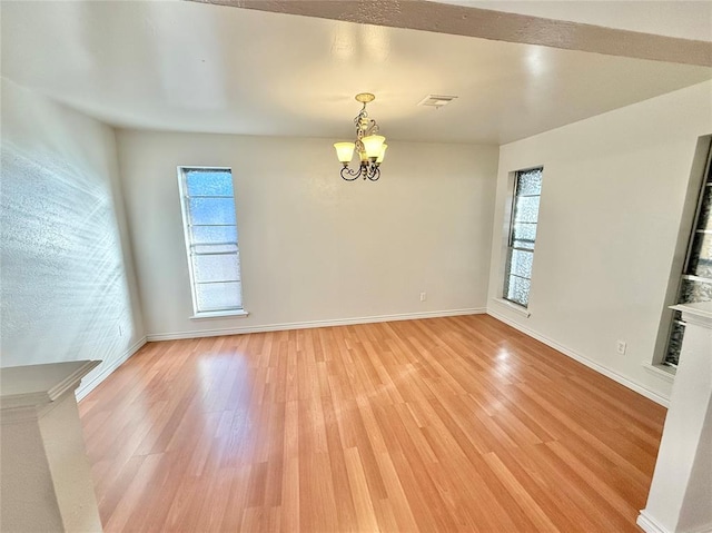 empty room with plenty of natural light, an inviting chandelier, and light hardwood / wood-style floors