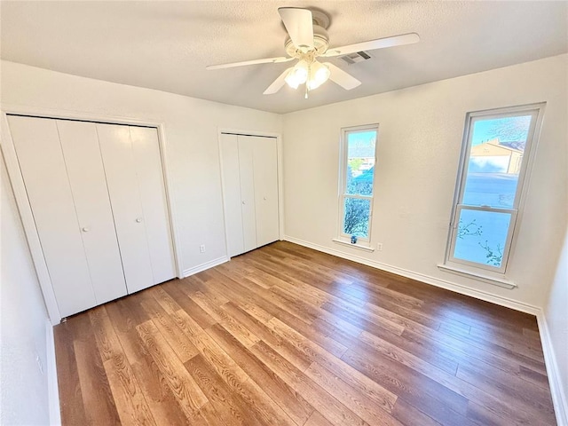 unfurnished bedroom featuring multiple windows, wood-type flooring, two closets, and a textured ceiling