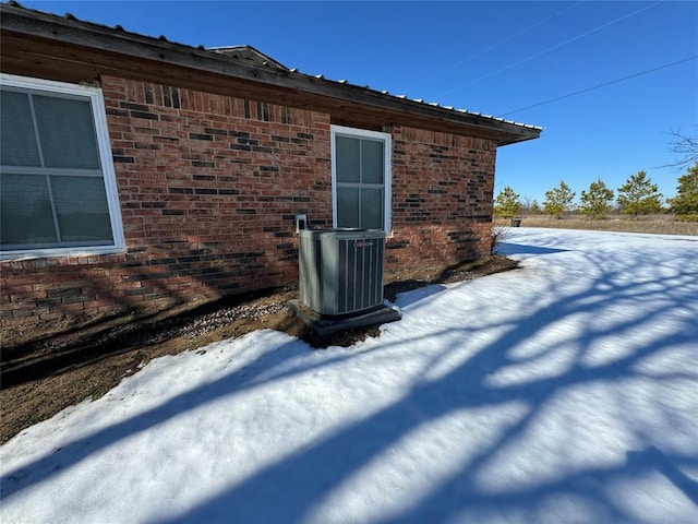 snow covered property with central AC unit and brick siding