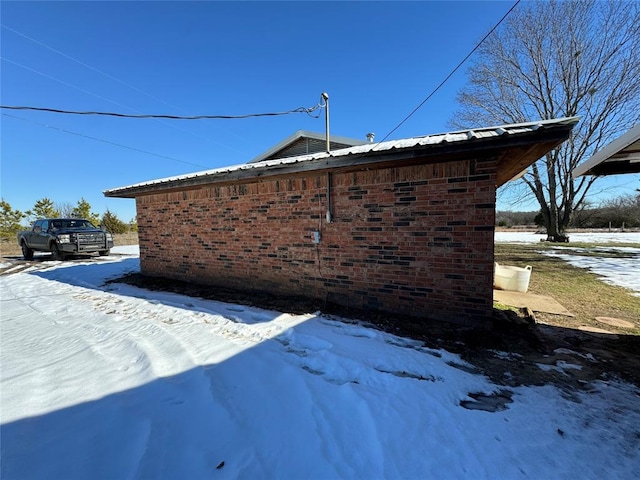 view of snowy exterior with metal roof and brick siding