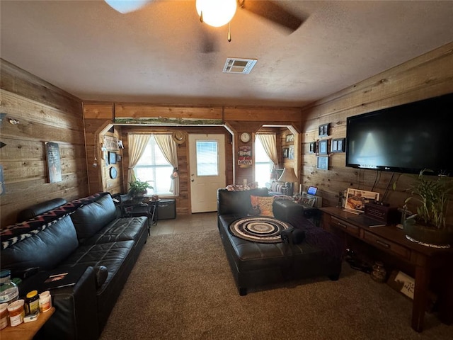 living area featuring a textured ceiling, wood walls, visible vents, and a ceiling fan