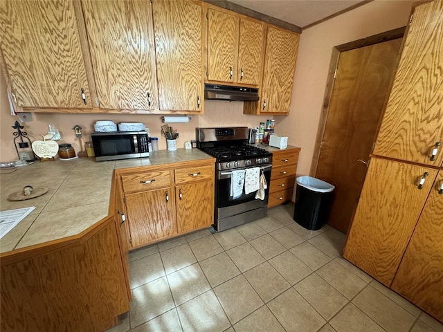 kitchen with light tile patterned floors, tile countertops, appliances with stainless steel finishes, brown cabinets, and under cabinet range hood