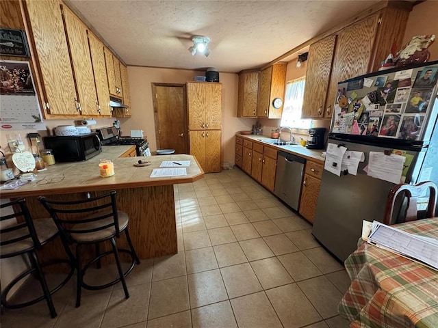 kitchen with light tile patterned floors, appliances with stainless steel finishes, a sink, a peninsula, and under cabinet range hood