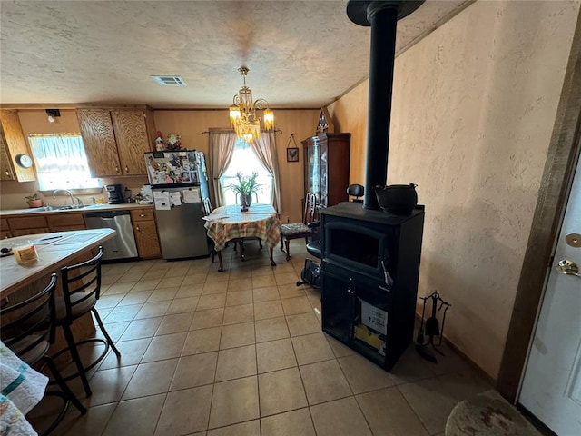 kitchen with brown cabinets, freestanding refrigerator, a wood stove, light tile patterned flooring, and dishwasher