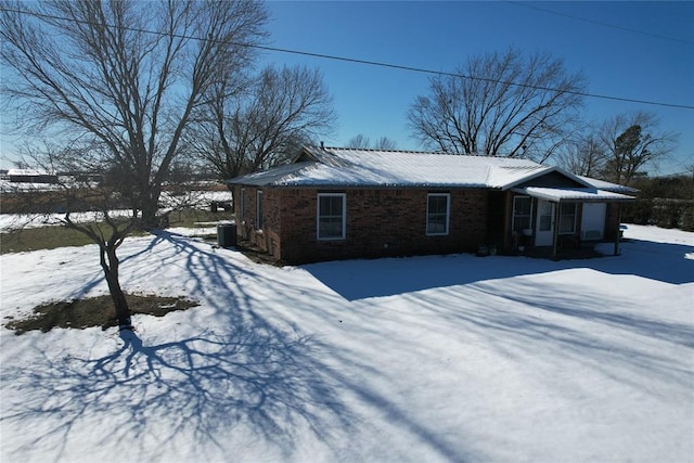 snow covered property featuring brick siding and central AC unit