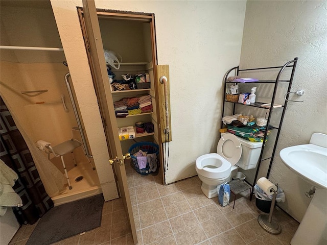 bathroom featuring a textured wall, tile patterned flooring, a shower stall, and toilet