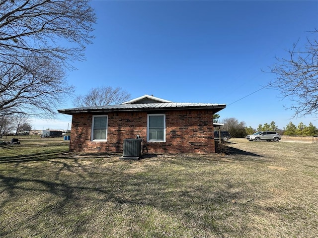 view of property exterior with metal roof, brick siding, a lawn, and central air condition unit