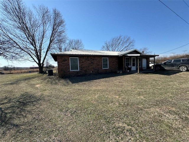 view of front of house with a front yard, brick siding, metal roof, and central air condition unit