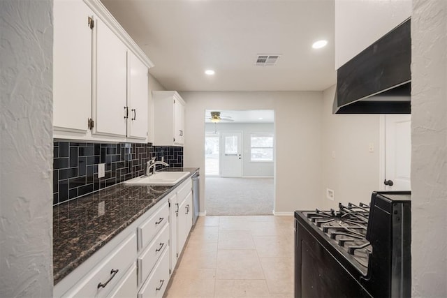 kitchen with light colored carpet, white cabinets, dark stone counters, ceiling fan, and black gas range