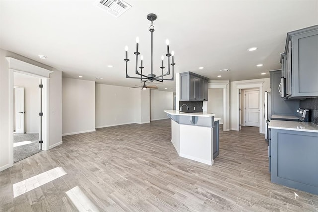 kitchen with an inviting chandelier, backsplash, hanging light fixtures, gray cabinets, and light hardwood / wood-style flooring