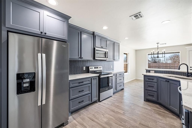 kitchen with light stone countertops, decorative light fixtures, stainless steel appliances, an inviting chandelier, and sink