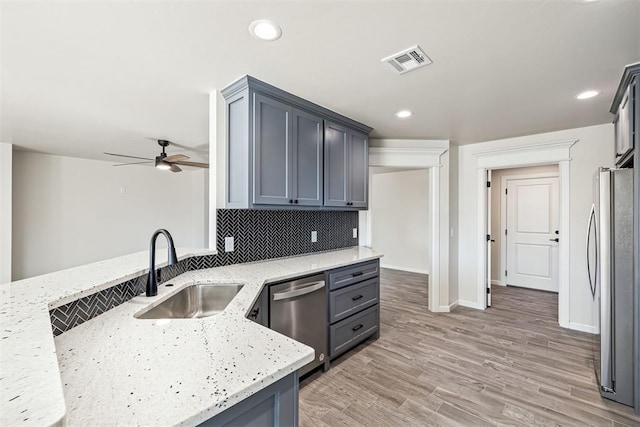 kitchen featuring stainless steel appliances, tasteful backsplash, ceiling fan, sink, and light stone counters