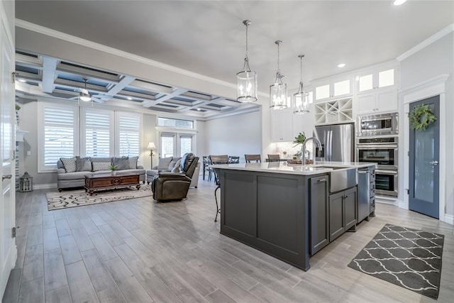 kitchen with a kitchen island with sink, stainless steel appliances, coffered ceiling, white cabinets, and decorative light fixtures