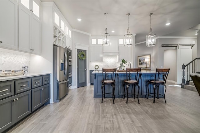 kitchen featuring stainless steel refrigerator with ice dispenser, tasteful backsplash, hanging light fixtures, a barn door, and white cabinets