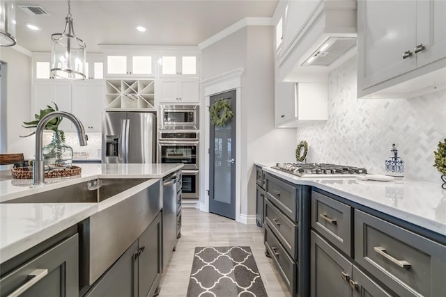 kitchen featuring custom exhaust hood, ornamental molding, appliances with stainless steel finishes, gray cabinets, and white cabinets