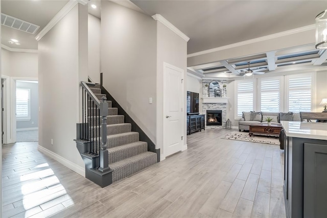 interior space with ceiling fan, coffered ceiling, ornamental molding, a tiled fireplace, and beamed ceiling