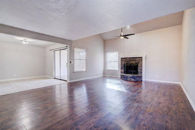 unfurnished living room with vaulted ceiling, light wood-type flooring, ceiling fan, a fireplace, and a textured ceiling