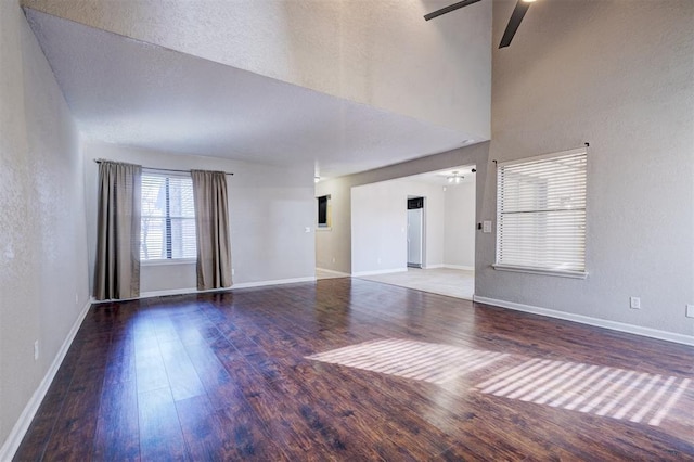 unfurnished living room with ceiling fan, a towering ceiling, and hardwood / wood-style flooring