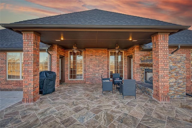 patio terrace at dusk with grilling area, ceiling fan, and exterior fireplace