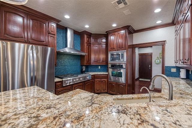 kitchen with light stone counters, wall chimney range hood, decorative backsplash, appliances with stainless steel finishes, and sink