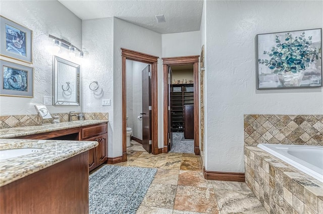 bathroom with toilet, vanity, a textured ceiling, and a relaxing tiled tub