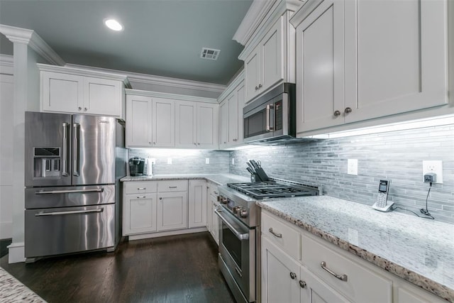 kitchen featuring high end appliances, white cabinetry, light stone counters, and tasteful backsplash