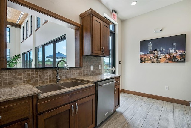 kitchen with a wealth of natural light, light stone countertops, sink, and stainless steel dishwasher