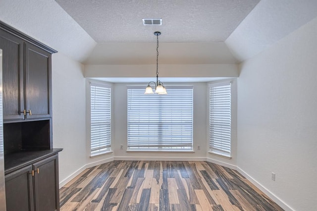 unfurnished dining area featuring dark hardwood / wood-style flooring, a textured ceiling, lofted ceiling, and a notable chandelier