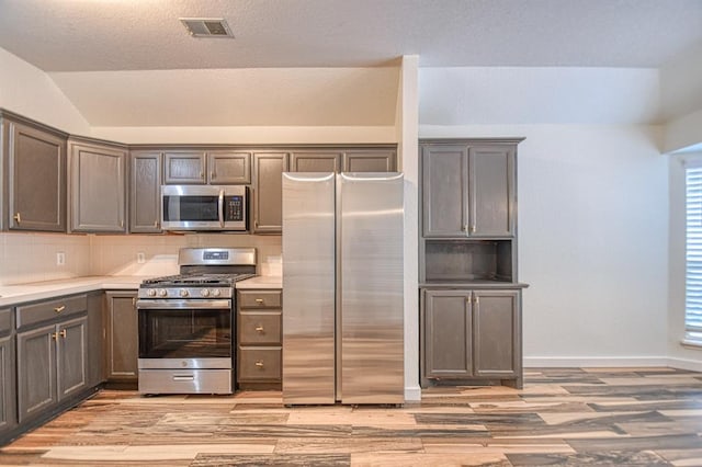 kitchen featuring backsplash, lofted ceiling, stainless steel appliances, and light hardwood / wood-style flooring