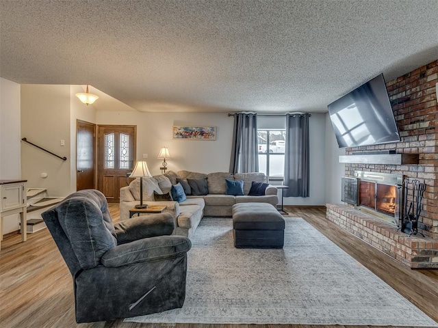 living room featuring a brick fireplace, a textured ceiling, and hardwood / wood-style flooring