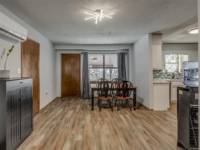 dining space featuring a textured ceiling, light hardwood / wood-style floors, sink, and a wall unit AC