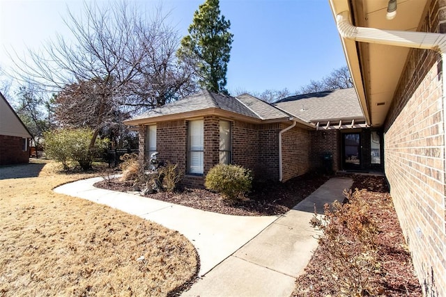 view of side of home featuring brick siding and a shingled roof