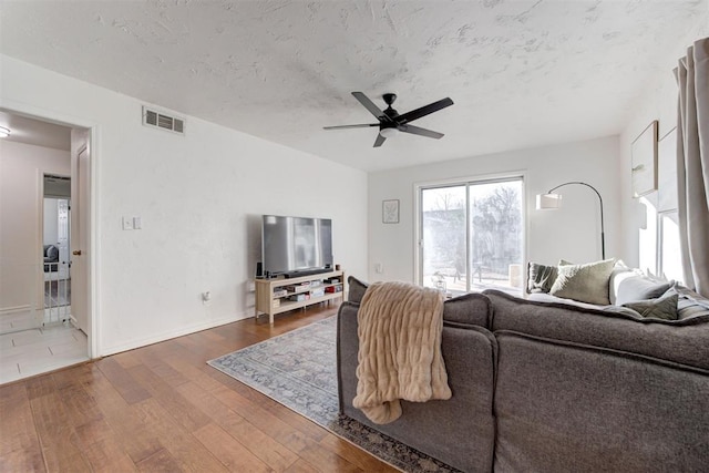 living room with a textured ceiling, ceiling fan, and wood-type flooring