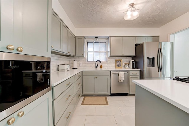 kitchen featuring appliances with stainless steel finishes, gray cabinets, backsplash, and sink