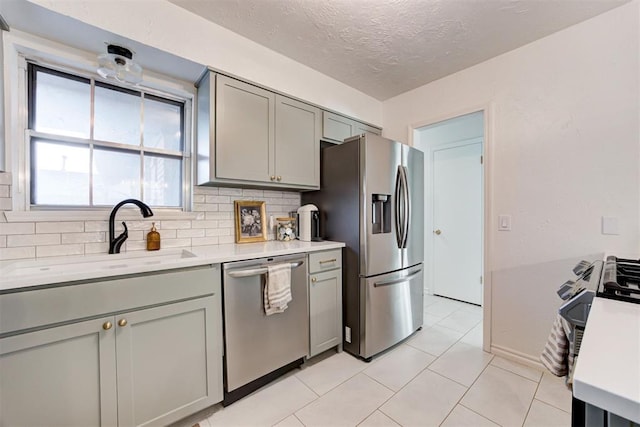 kitchen featuring a textured ceiling, stainless steel appliances, decorative backsplash, gray cabinets, and sink