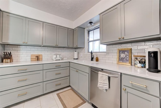 kitchen featuring sink, light tile patterned floors, stainless steel dishwasher, decorative backsplash, and gray cabinets