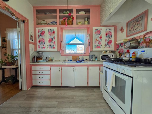 kitchen with sink, white cabinetry, white gas range, light wood-type flooring, and pendant lighting