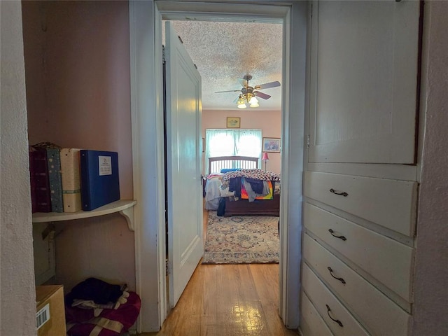 hallway with a textured ceiling and light hardwood / wood-style flooring