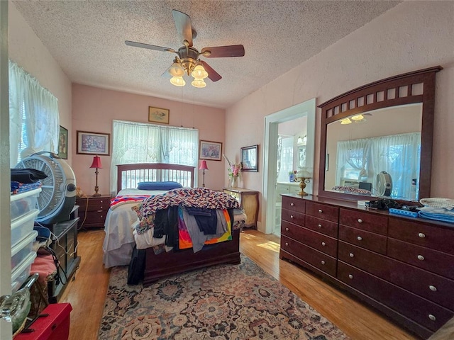 bedroom with ceiling fan, light wood-type flooring, ensuite bath, and a textured ceiling