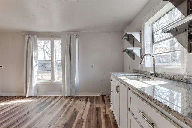 kitchen featuring light stone countertops, sink, white cabinets, and light hardwood / wood-style flooring