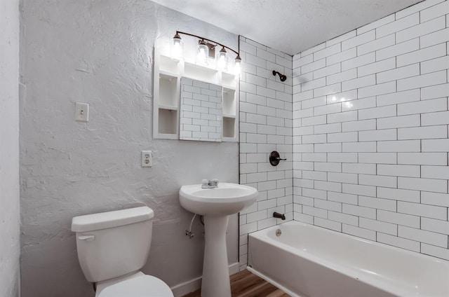 bathroom with tiled shower / bath, toilet, hardwood / wood-style floors, and a textured ceiling