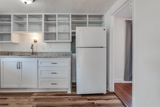 kitchen featuring wood-type flooring, sink, white cabinets, white refrigerator, and light stone counters