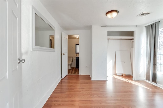 unfurnished bedroom with a closet, ensuite bath, and light hardwood / wood-style flooring