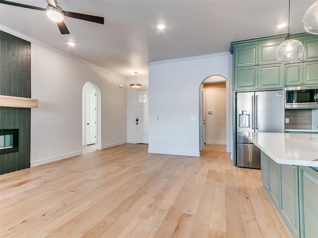 kitchen featuring crown molding, a tile fireplace, appliances with stainless steel finishes, green cabinetry, and light wood-type flooring