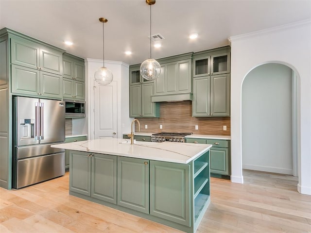 kitchen featuring stainless steel appliances, crown molding, hanging light fixtures, green cabinets, and an island with sink